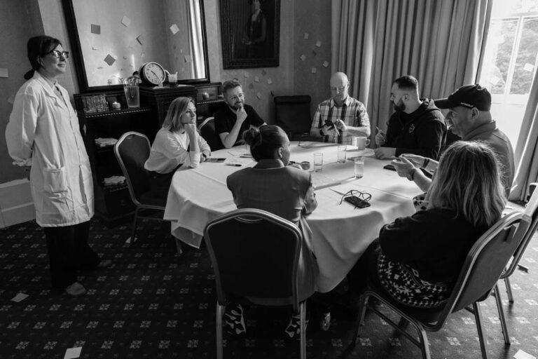 A grayscale photo of a diverse group of professionals engaged in a Learning & Development session around a table.