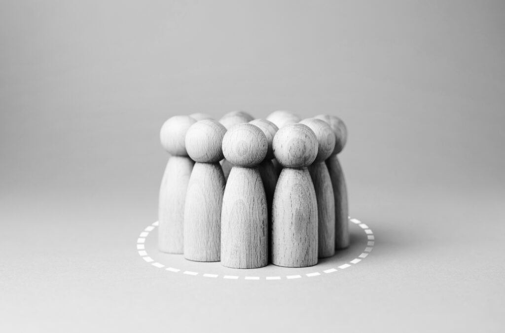 A group of wooden pegs, representing people, are huddled together inside a circle, making 360 degrees.