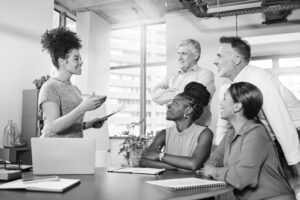 A female leader addresses a group of colleagues in an office.