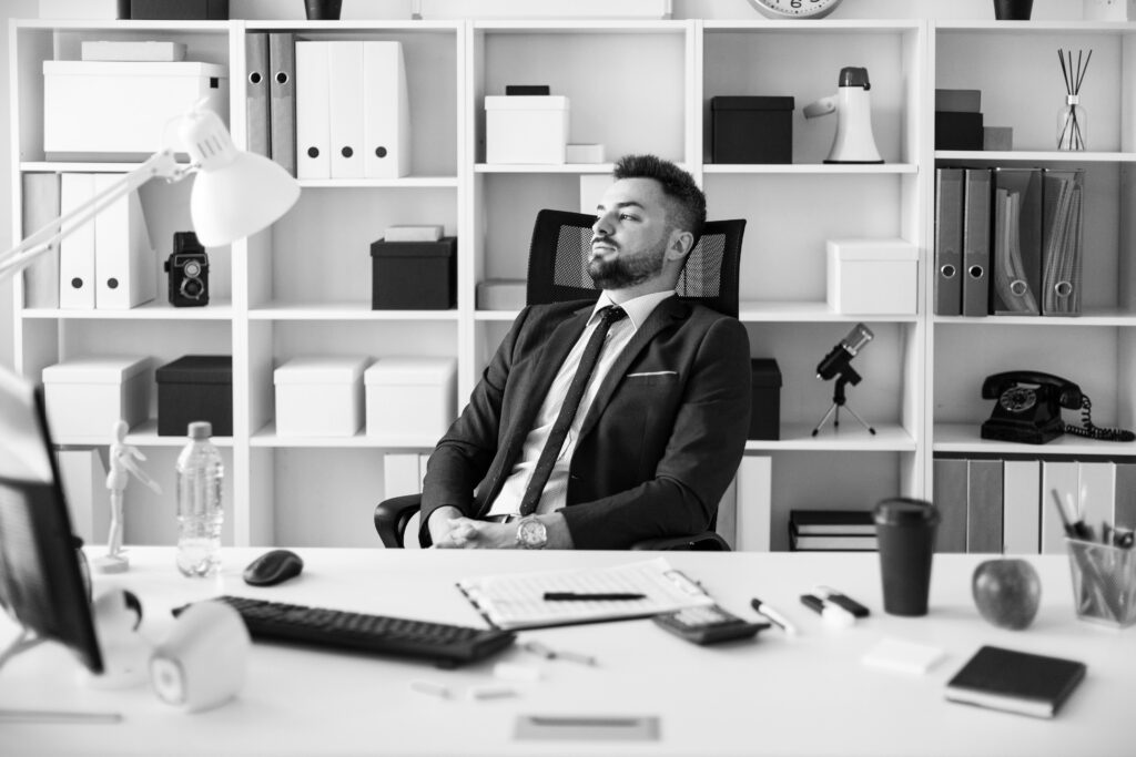 A man sits at his desk, dressed in a suit, gazing out of the window.