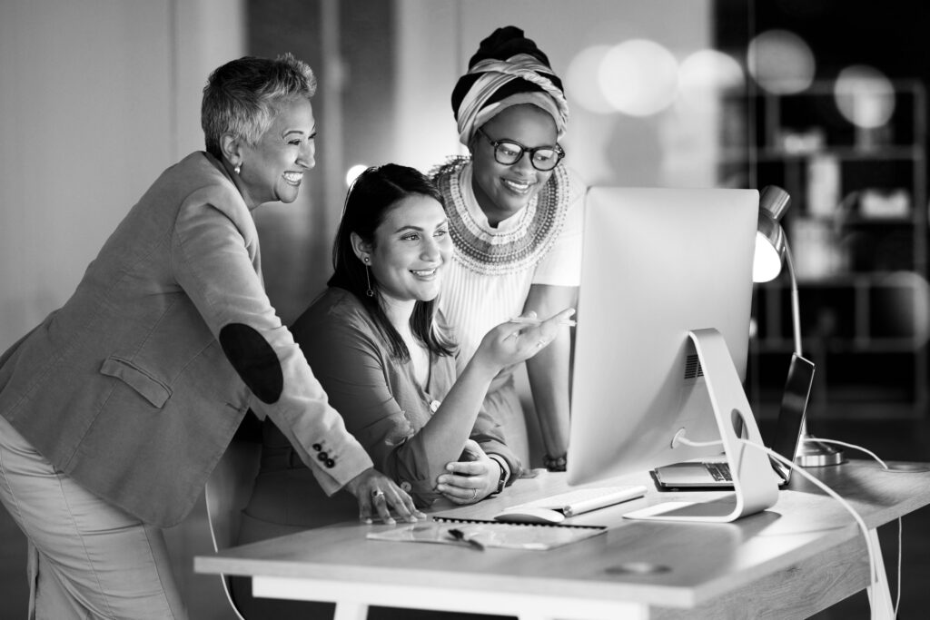 A group of female colleagues gather around a compute screen.